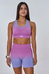 Conjunto deportivo compuesto por un top y un short de ciclismo, ambos con diseño degradado que transiciona de fucsia a lila. El top presenta cuello redondo y logo 'bk.' estampado en el frente, mientras que el short es de tiro alto y ajuste ceñido.