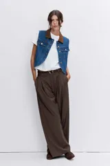 Chaleco de denim azul con cuello camisero en contraste color marrón, cierre frontal con botones metálicos y bolsillos superiores con solapa.