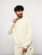 Buzo de felpa color crema, con cuello redondo, manga larga tipo raglán y puños y dobladillo acanalados. Incluye una etiqueta con el logo de Umbro en la parte delantera.