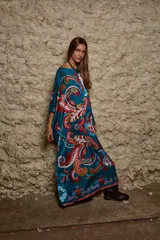 Vestido largo de seda estampado con motivos paisley en tonos turquesa, rojo y naranja. Tiene cuello bote, corte recto y aberturas laterales. Incluye un pañuelo al cuello con el mismo estampado.