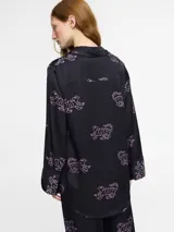 Camisa de manga larga confeccionada en seda viscosa, con cuello clásico y cierre frontal de botones. Presenta un estampado original de figuras de tigres en color rosado sobre fondo negro.