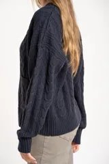 Cardigan de punto texturado con diseño de ochos, color azul marino, con escote en V, cierre frontal con botones dorados y mangas largas con puños acanalados.