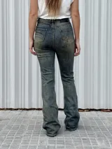 Jean de tiro alto con corte levemente oxford en la botamanga. Presenta un lavado vintage con efecto gastado, detalles de tachas metálicas en la zona de la cintura y a lo largo de las piernas.