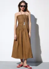 Vestido midi de ramio color marrón, sin tirantes con escote palabra de honor, diseño plisado en el corpiño y falda evasé.