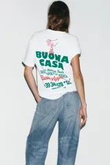 Camiseta blanca de manga corta y cuello redondo con estampado frontal en verde y rojo que dice "IL FORNELLO RUSTICO BUONA CASA Buon Appetito! - SINCE 1975 -".