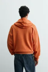 Sudadera tipo hoodie de corte relajado, confeccionada en tejido de algodón con textura estructurada y efecto lavado. Presenta cierre frontal con cremallera, cuello con capucha, manga larga, bolsillos tipo canguro y acabados en rib.