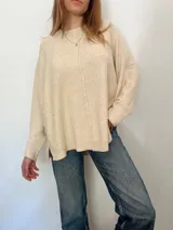 Sweater oversize de tejido liviano, color beige, con cuello redondo, mangas largas con puños acanalados y tajos laterales. Presenta una costura vertical decorativa en el frente y un diseño más largo en la parte posterior.