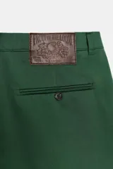 Bermuda de tiro medio color verde oscuro, con trabillas en la cintura, bolsillos laterales y detalle de pliegues delanteros. Presenta un bajo con acabado asimétrico y cierre frontal con cremallera, botón interior y ganchos metálicos. Colección especial Fruit of the Loom con Zara.
