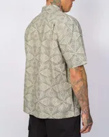 Camisa de manga corta color verde con estampado geométrico, cierre frontal con botones y un bolsillo en el pecho.