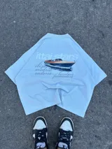 Remera celeste de corte recto con estampado de un yate y texto en color gris.