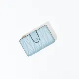 Billetera pequeña color celeste con diseño acolchado geométrico y cierre con broche a presión.