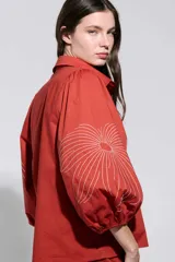 Camisa roja con bordados florales blancos, cuello camisero, cierre frontal oculto y mangas largas abullonadas.