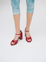 Sandalias de taco alto ancho con diseño retro, confeccionadas en charol negro. Presentan tiras delanteras múltiples entrelazadas, talón cerrado y una correa fina ajustable al tobillo con hebilla metálica.
