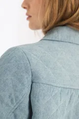 Chaqueta capitoneada celeste vintage de denim de algodón 100% natural pre-lavado y suavizado, con bolsillos laterales, botones a presión escondidos y ruedo curvo en los costados.