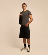 Bermuda baggy de jean color negro con pespuntes contrastantes, cierre de botón y cremallera, y bolsillos.