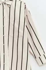 Vestido camisero largo con estampado de rayas verticales negras y crudas, corte recto, manga larga con puños y bolsillo en el pecho.