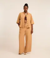 Pantalón de sarga de corte ancho tipo pantalona, color tostado, con cintura fija, trabillas, elástico trasero y cinturón incorporado con hebilla redonda.