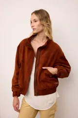 Chaqueta de gamuza color marrón con cierre frontal, cuello alto y puños elásticos. Presenta un diseño de espíritu artesanal con apliques bordados en los bolsillos delanteros y en la espalda, y se encuentra completamente forrada.