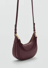Bolso de hombro tipo hobo en color bordó, con diseño de media luna y acabado efecto piel. Cuenta con cierre de cremallera superior, herrajes metálicos dorados y asa de hombro ajustable y extraíble.