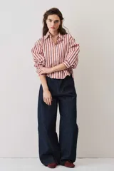 Camisa a rayas verticales en tonos rosado y marrón, de manga larga abullonada, cuello camisero y cierre frontal de botones con pequeños apliques brillantes.