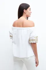 Blusa blanca con escote bardot y mangas cortas abullonadas con bordados dorados.