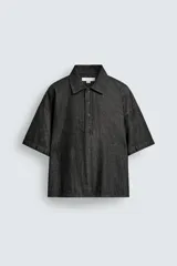 Camisa de manga corta con cuello solapa y cierre frontal de botones. Confeccionada en tejido denim de algodón, de corte relajado y aberturas laterales en el bajo.