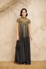 Capa negra con cuello alto y bordados dorados. Presenta flecos largos dorados que caen desde los hombros.