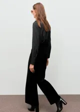 Pantalón de terciopelo negro de tiro medio y diseño wide leg con cinco bolsillos, cierre de botón y cremallera, y trabillas para cinturón.