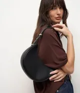Bolso baguette en formato media luna, con correa de hombro ajustable mediante detalles metálicos y cierre superior por cremallera. Diseño minimalista con acabado liso.