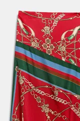 Falda midi de tiro medio con bajo asimétrico y cierre posterior con cremallera oculta. Presenta un diseño fluido con estampado de cadenas, borlas y motivos ecuestres sobre fondo rojo, con bordes en tonos verde y azul.