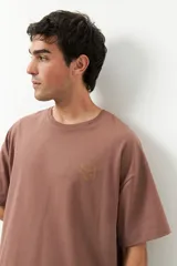 Remerón unisex color marrón claro, de manga corta y cuello redondo, con pequeño estampado lateral en el frente y otro grande en la espalda.