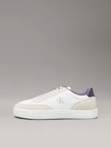 Zapatillas de corte bajo Calvin Klein, con diseño minimalista en color blanco y beige. Presentan una combinación de materiales en la capellada, incluyendo piel y ante, con detalles en contraste en el talón y logo de la marca en el lateral y la mediasuela.