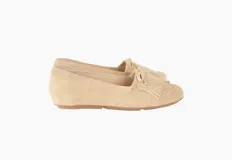 Mocasines de cuero gamuzado color avena, con flecos en la capellada y un lazo frontal con herrajes metálicos dorados. El interior está forrado en cuero y la suela es de goma flexible.