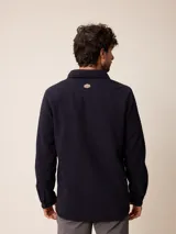 Sobrecamisa de polar azul marino con cierre frontal de botones a presión. Presenta bolsillos frontales con solapa, uno de ellos con cierre de cremallera adicional y detalles en contraste de material técnico.