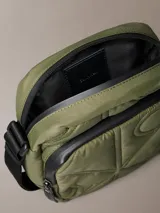 Cartera reporter color verde militar de Calvin Klein, con textura acolchada, costuras con monograma, cierre superior y bolsillo delantero con cremallera. Incluye correa ajustable negra.