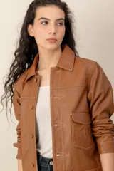 Campera de cuero marrón, con cuello camisero, cierre frontal con botones metálicos y bolsillos frontales.