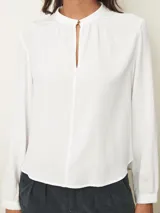 Blusa de manga larga color blanco, con cuello mao y abertura frontal tipo gota con cierre de botón. Presenta un diseño fluido con frunces en el escote y puños abotonados.