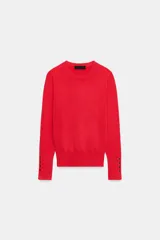 Jersey de punto liso color rojo, con cuello redondo, manga larga y detalle de botones metálicos en los puños.