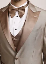 Traje formal de tres piezas en tono tostado brillante, compuesto por saco con solapas en contraste, pantalón de corte recto y chaleco a juego, acompañado de moño.