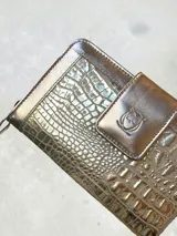 Billetera grande de cuero con acabado metalizado dorado y textura tipo reptil. Cuenta con un compartimento frontal con solapa y cierre a presión, decorado con el logo de la marca grabado.