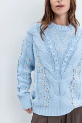 Sweater de punto color celeste, con diseño de trenzas y detalles de cordones entrelazados en el frente y las mangas. Presenta cuello redondo y puños acanalados.