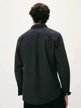 Camisa de manga larga con cuello clásico, cierre frontal de botones y bolsillo en el pecho. Presenta un diseño de rayas verticales finas en tonos azul y blanco.