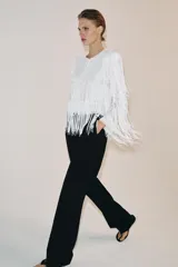 Chaqueta de cuello redondo y manga larga con hombreras, completamente cubierta de flecos con lentejuelas. Cuenta con forro interior y cierre frontal.
