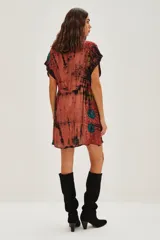 Vestido midi de viscosa con escote en V profundo, mangas cortas tipo kimono y cintura elástica con lazo ajustable. Presenta un estampado tie-dye en tonos rojizos, negros y toques de verde, con aplicaciones decorativas brillantes.