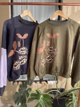 Buzo cropped de algodón color verde militar, con mangas ranglan y diseño estampado en el frente con motivos de besos y moños. Cuenta con elástico holgado en la cintura y los puños.