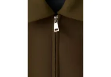Chaqueta color verde militar, de corte recto con cierre frontal de cremallera, cuello camisero y bolsillos laterales.