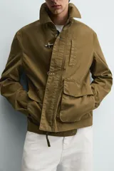 Parka de corte relajado confeccionada en mezcla de algodón color marrón. Presenta cuello solapa, cierre frontal con cremallera oculta y alamares metálicos, bolsillos de plastrón con solapa en la cadera y bolsillo de vivo en el pecho.