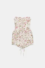 Vestido corto strapless de corte corsetero, con estampado floral en tonos rosados y verdes sobre fondo blanco. Presenta detalles de tiras cruzadas ajustables en el delantero con lazada y varillas interiores.