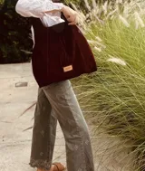 Cartera tipo hobo de gamuza color borgoña con flecos y asa corta de cuero marrón.