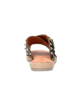 Sandalia tipo ojota con base de yute, tiras cruzadas de cuero negro con tachas doradas y hebilla metálica decorativa.